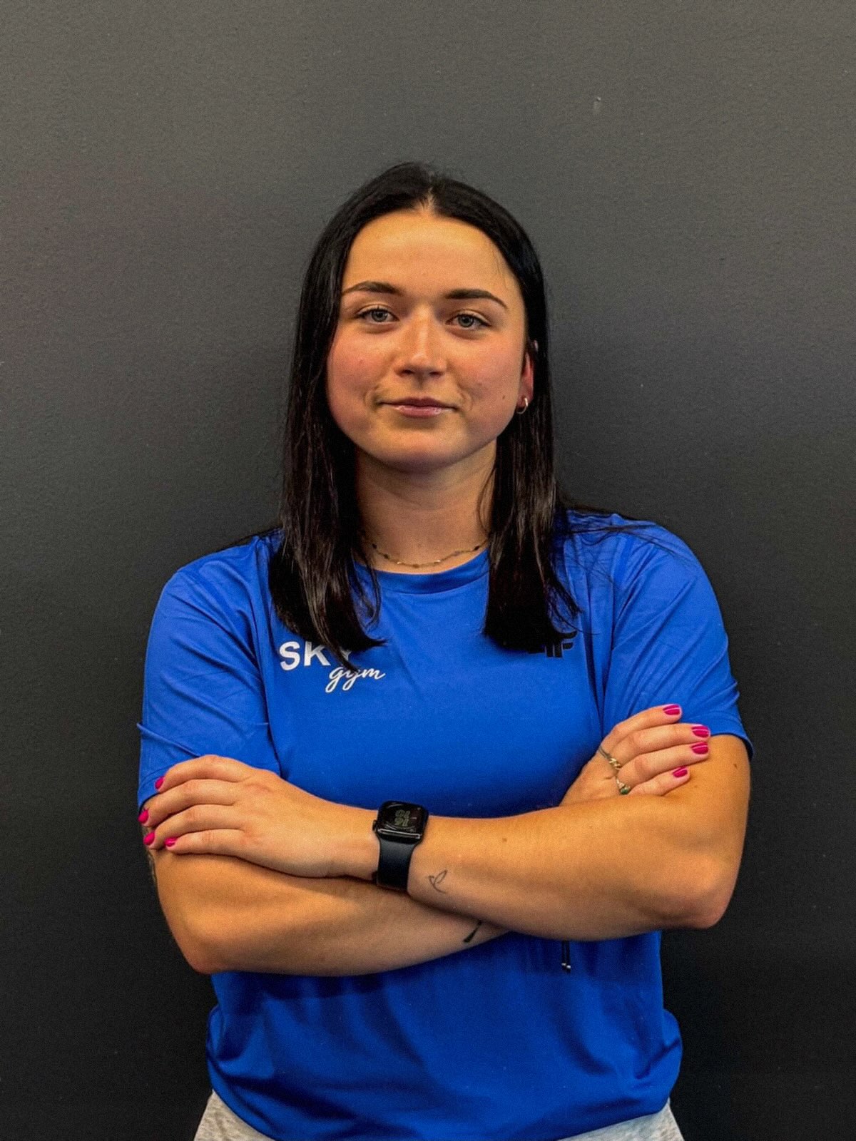 Karolina Błaszczyk w niebieskiej koszulce SKY gym, z założonymi rękami