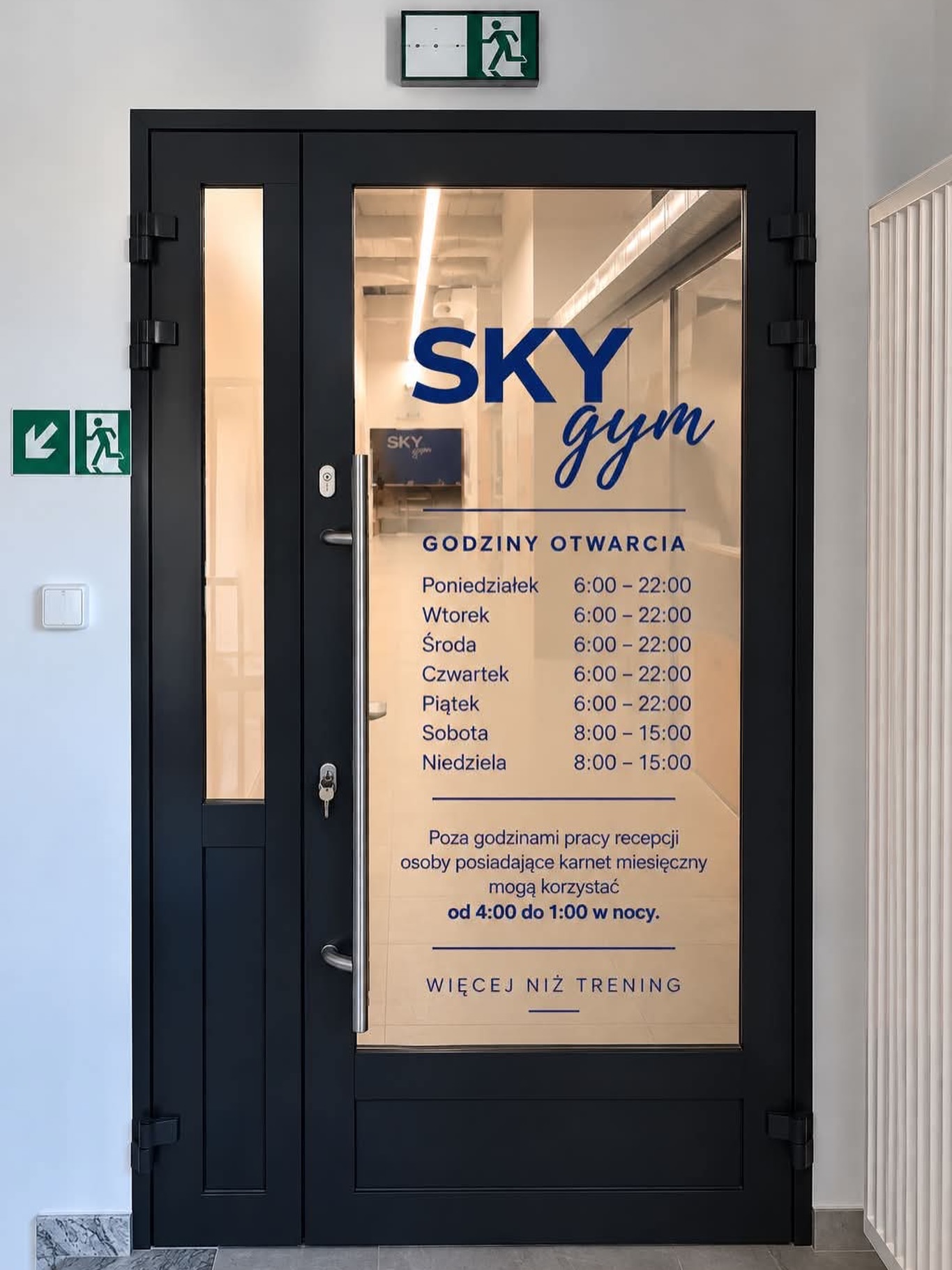 Drzwi wejściowe SKY gym z logo i rozpiską godzin otwarcia na szybie